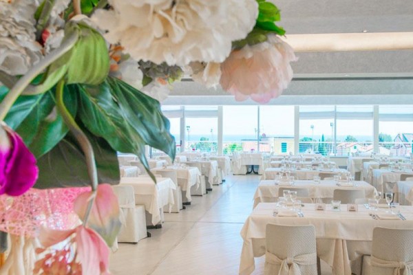 Elegantní restaurace s bílými ubrusy a výhledem na venkovní terasu skrze velká okna.