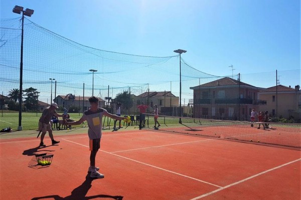 Lidé hrají tenis na venkovním kurtu za slunečného dne.