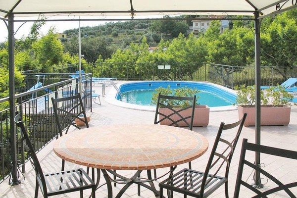 Pergola s kulatým stolem a židlemi u venkovního bazénu na terase.