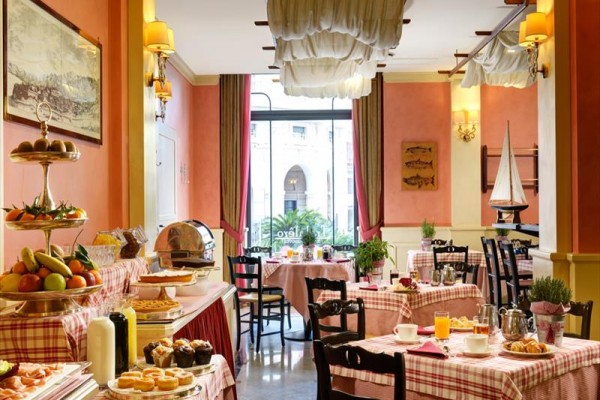 Světlá restaurace s dřevěnými stoly pokrytými kostkovanými ubrusy a bufetovým stolem plným jídla.