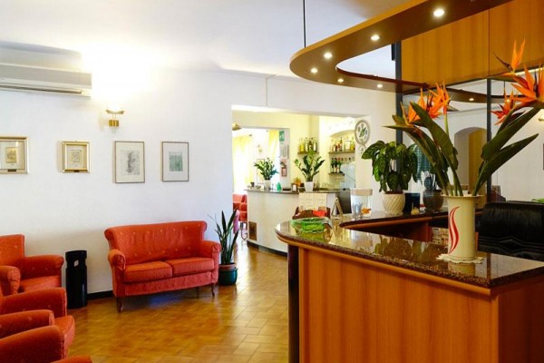 Recepce hotelu s dřevěným pultem, květinami a červeným nábytkem.