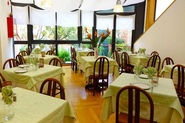 Interiér restaurace s dřevěnými židlemi a ubrusy ve světle zelené barvě.