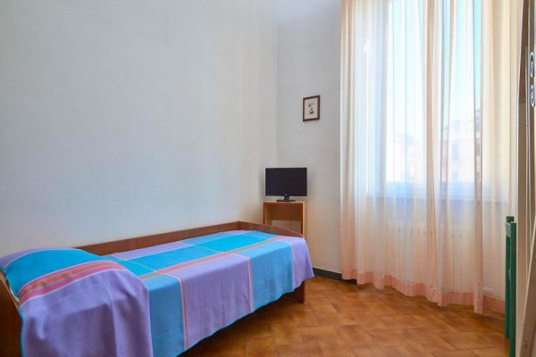 Jednolůžkový pokoj s modro-růžovým přehozem a malou televizí u okna s průsvitnými záclonami.