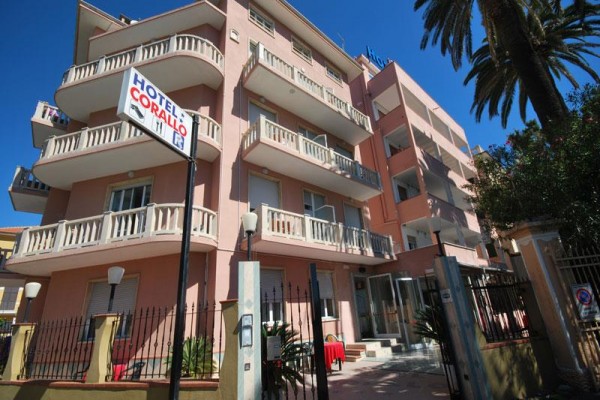 Růžový hotel s několika balkony a palmou vedle vstupu.