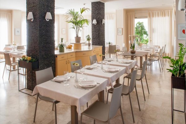 Moderní restaurace s prostřenými stoly a světlým interiérem, zdobená rostlinami.