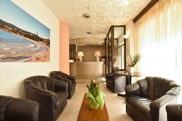 Předsálí hotelu s recepcí, koženými křesly a květinami na stole.