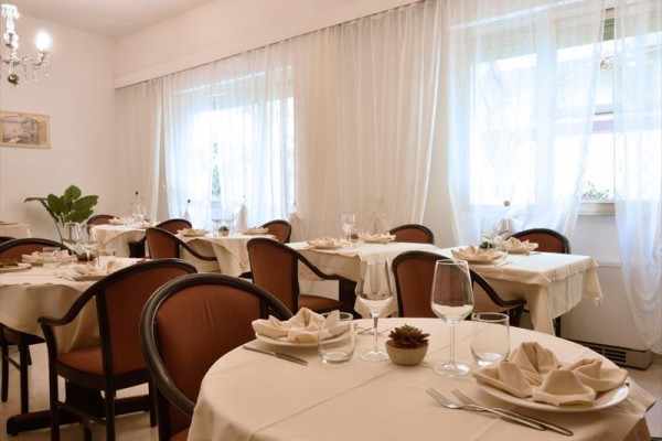 Elegantně prostřená jídelna s kulatými stoly a židlemi, zdobená světlými ubrusy a sklenicemi.