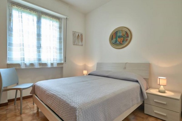 Světlá ložnice s dvojlůžkem, nočními stolky a obrazem na zdi.