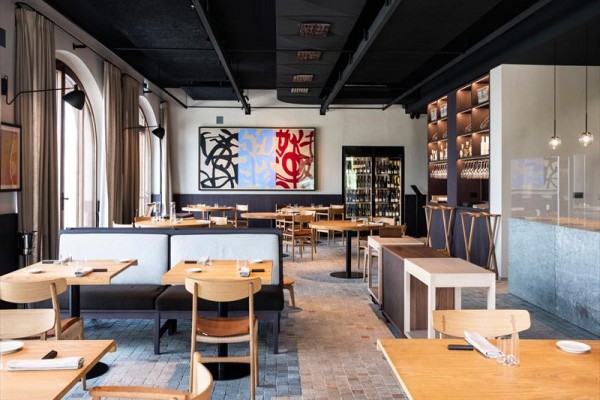 Moderní restaurace s dřevěným nábytkem a abstraktními obrazy na stěně.