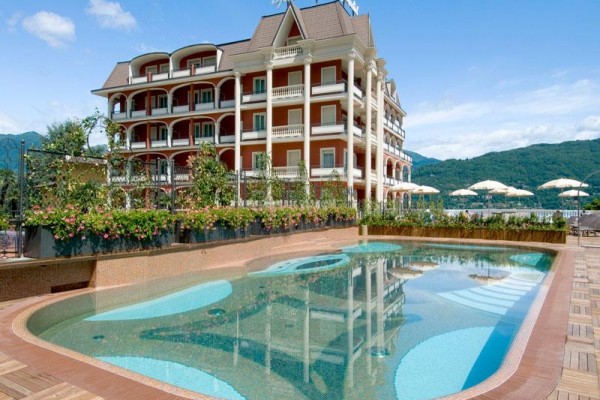 Luxusní hotel s bazénem a horami v pozadí pod modrou oblohou.