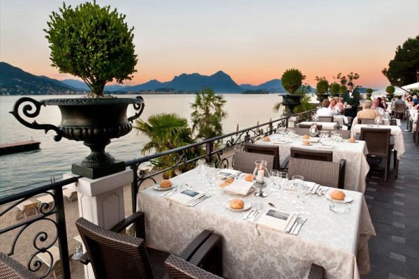 Restaurace na terase s výhledem na jezero a hory při západu slunce.  