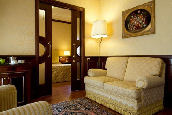 Elegantní obývací pokoj s pohovkou, lampou a obrazem na stěně, vedoucí do ložnice.