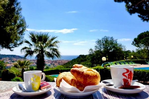 Šálky kávy a croissanty na stole s výhledem na krajinu u moře.