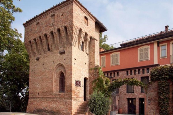 Historická cihlová věž s přilehlou budovou porostlou zelení.  