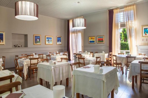 Restaurace s dřevěnými židlemi a stoly pokrytými bílými ubrusy, s obrazy na stěnách.