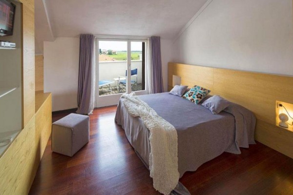 Moderní ložnice s velkou postelí a balkónem s výhledem na trávník.