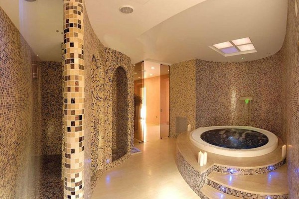 Luxusní interiér spa s vířivkou a stěnami obloženými mozaikovými dlaždicemi.