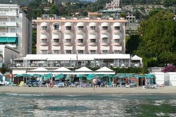 Růžová budova hotelu se slunečníky a lehátky na pláži.
