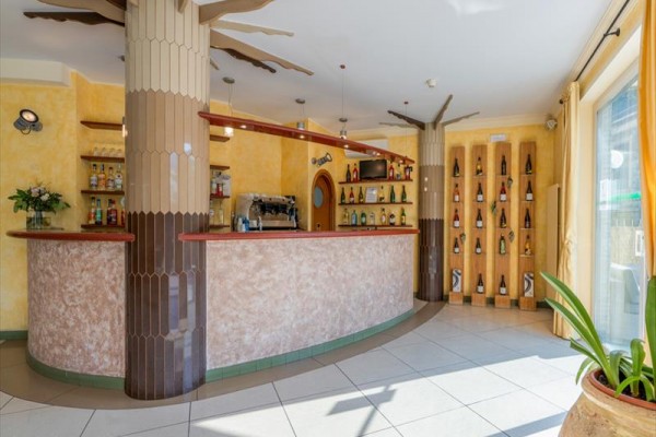 Stylový bar s dřevěnými dekoracemi a vystavenými lahvemi alkoholu na žluté stěně.