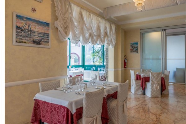 Restaurace s prostřenými stoly, bílými ubrusy a červenými doplňky.
