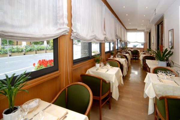 Restaurace s prostřenými stoly a okny s bílými závěsy.