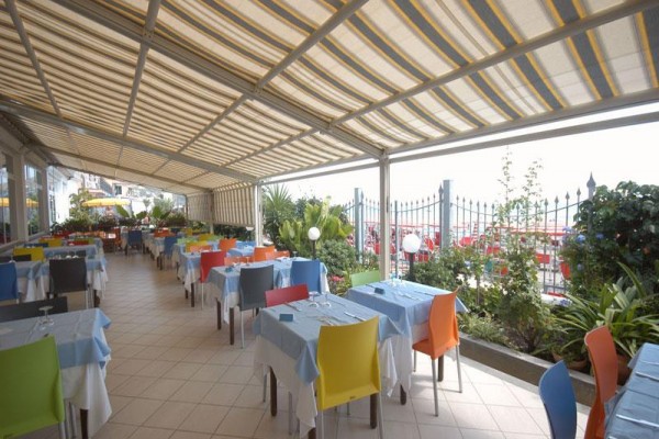Venkovní terasa restaurace s barevnými židlemi a stolky pokrytými modrými ubrusy.