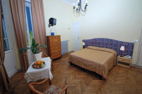 Ložnice se žlutými zdmi, postelí, komodou, stolem s ovocem a křeslem.