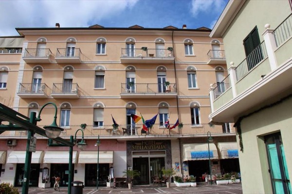 Budova hotelu s balkony a vlajkami u vchodu.