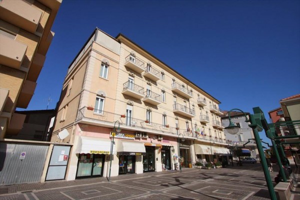 Budova s obchody v přízemí a balkóny nad nimi na pozadí modré oblohy.