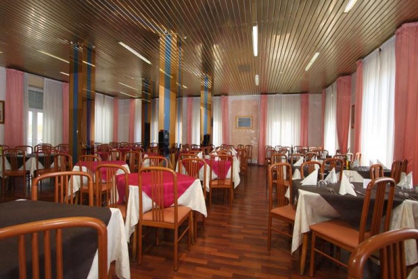 Restaurace s dřevěnými stoly, židlemi a bílými závěsy.