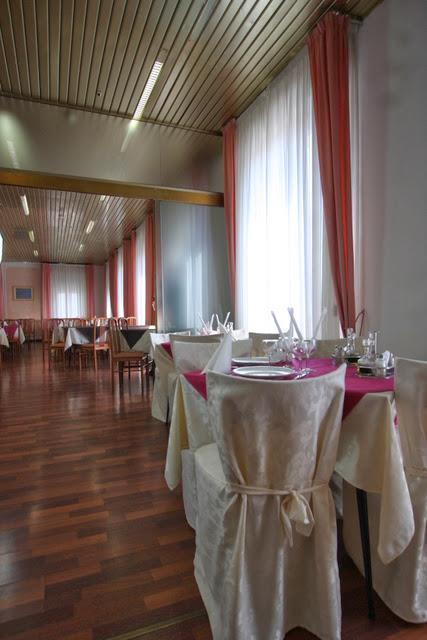 Restaurace s dekorovanými stoly, bílými židlemi a růžovými závěsy.