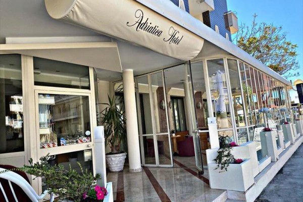 Vstup do hotelu s markýzou a květinami v květináčích.