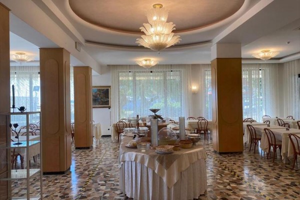 Elegantní restaurace s kulatými stoly, dřevěnými židlemi a stropními svítidly.  