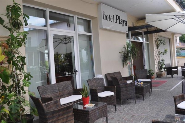Venkovní posezení hotelu s ratanovým nábytkem pod markýzou.