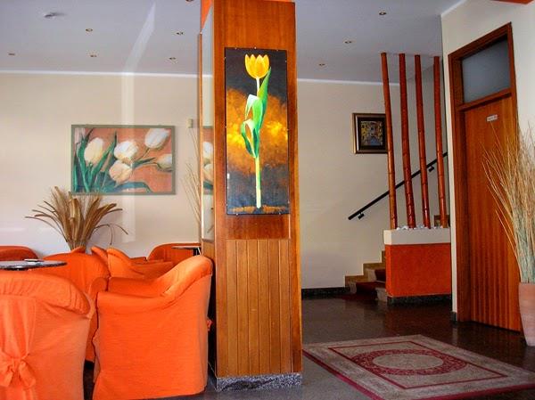 Hotelová lobby s oranžovými křesly a obrazy květin na stěnách.