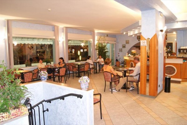 Lidé sedící u stolů v restauraci s modrými stěnami a velkými okny.