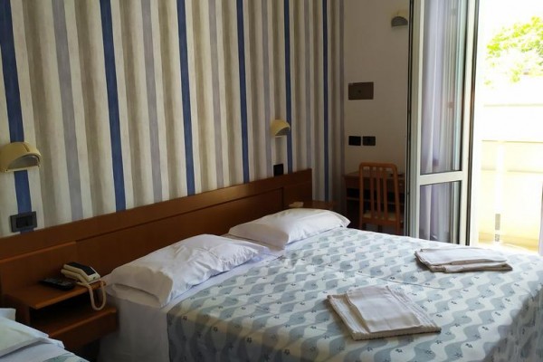 Pokoj s dvěma postelemi, pruhovanými tapetami a otevřenými dveřmi na balkon.