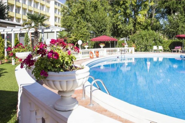 Bazén obklopený zelení a květinami u hotelu.
