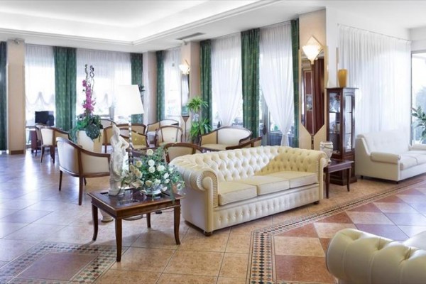 Elegantní hotelové lobby s bílými pohovkami a zelenými závěsy.
