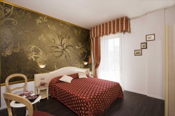 Elegantní hotelový pokoj s dvoulůžkem a výraznou zlatou tapetou.