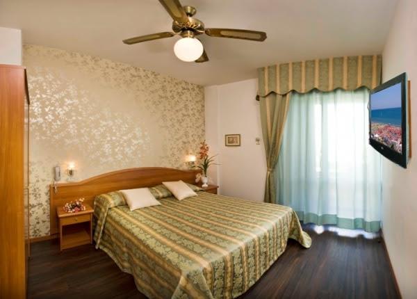 Komfortní ložnice s manželskou postelí, stropním ventilátorem a televizí na stěně.
