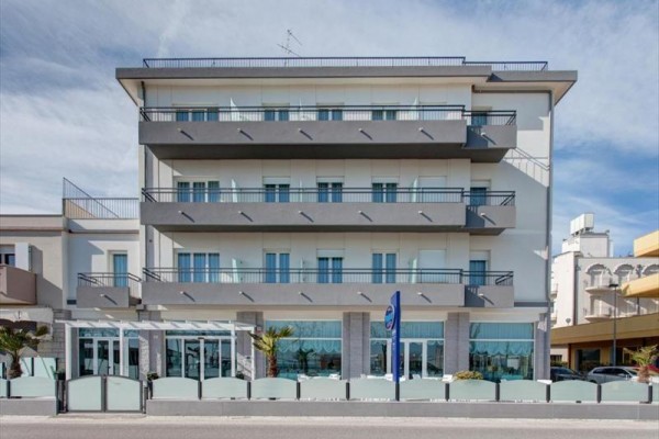 Čtyřpodlažní moderní budova s balkóny a velkými okny.