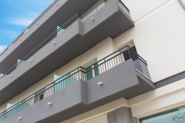 Moderní budova s tmavými balkóny a modrým nebem na pozadí.