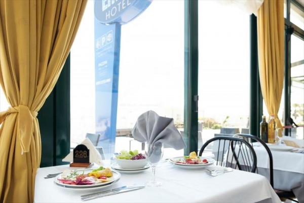 Stolky v restauraci s prostřeným ubrusem a elegantně složeným ubrouskem, vedle okna s výhledem ven.
