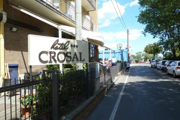 Cedule hotelu Crosal u silnice s auty a stromy.