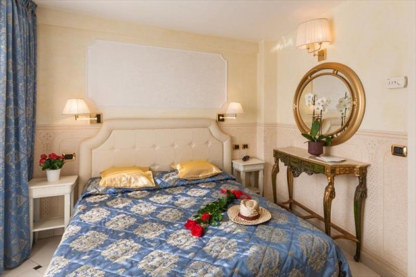 Luxusní ložnice s manželskou postelí, zdobeným povlečením a zrcadlovým stolkem s orchidejí.