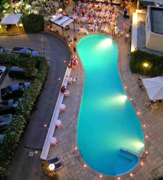 Pohled shora na osvětlený venkovní bazén obklopený stoly a židlemi hotelové restaurace.