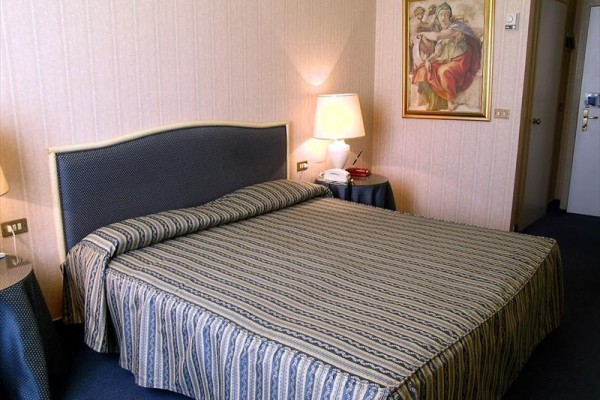 Elegantní hotelový pokoj s dvoulůžkem, lampou a obrazem na zdi.  