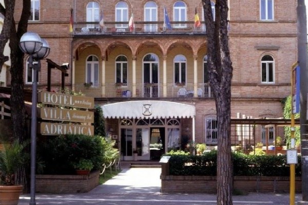 Hotel Villa Adriatica s cihlovou fasádou a balkony, obklopený stromy.