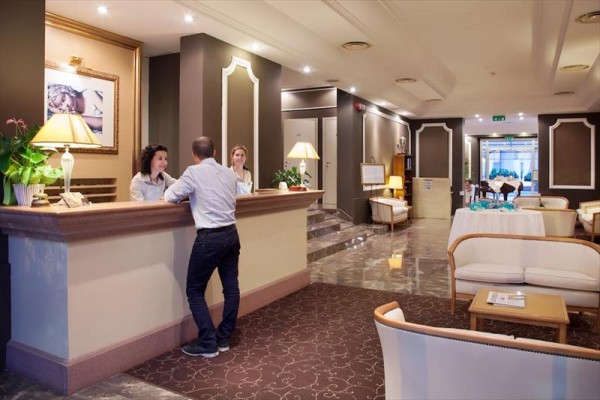 Recepce hotelu s dvěma pracovníky a jedním hostem.